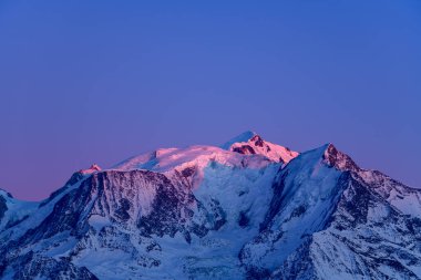 Mont Blancs 'ın buzlu zirvesi ve engebeli tepeleri, koyu mavi gökyüzüne karşı yumuşak mor alacakaranlıkla aydınlanır ve karmaşık buzullar ortaya çıkar..