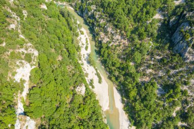 Yüksek açılı insansız hava aracı görüntüsü yoğun yeşil orman ve Verdon Boğazı 'ndaki kayalık yamaçlarla çevrili dolambaçlı bir nehir yatağını gün ışığında ortaya çıkardı..