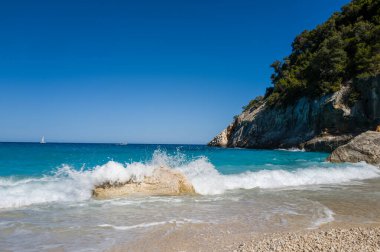 Köpüklü bir dalga, Cala Goloritze, Sardunya 'nın çakıllı sahilinde, turkuaz su ve engebeli kayalıklara çarpıyor..