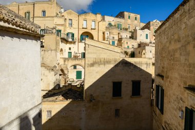 Sıcak güneş ışığı, Matera, İtalya 'nın tarihi merkezinde yeşil kepenkleri ve katmanlı mimarisi olan dokulu kireçtaşı binalar boyunca geometrik gölgeler oluşturur..