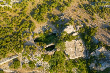 Engebeli kayalar ve yeşil çalılarla çevrili antik taş kalıntılarının tepeden tırnağa insansız hava aracı görüntüsü, Château de Opoul Perillos yakınlarındaki kurak bir arazide geçiyor..