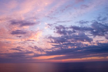 Yumuşak lavanta ve şeftali bulutları, gün batımında sakin bir Akdeniz 'de süzülür. Hafif ışık suyu yansıtır ve barışçıl, atmosferik bir hava yaratır..