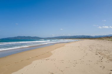 Kumihamacho 'daki Shotenkyo Sahili boyunca uzanan geniş kumlu bir sahil, açık gökyüzünün altında hafif sörf ve uzak mavi dağlarla kaplı. Kumda ayak izleri açık kıyılara sessiz bir yalnızlık hissi katar..