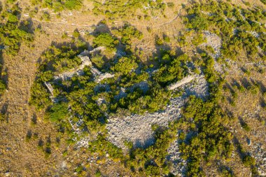 Yıpranmış taş kalıntılarının hava görüntüsü kısmen yoğun yeşil çalılar ve kuru otlarla kaplı, sıcak güneş ışığıyla aydınlatılmış, Opoul Şatosu yakınlarındaki engebeli bir yamaçta..