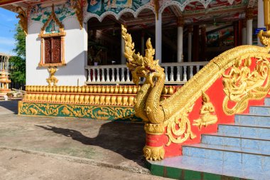 Laos, Vientiane 'deki bir Budist tapınağındaki kırmızı ve mavi merdiven kenarı birden fazla başlı altın naga ile süslenmiştir. Sabah güneşi, karmaşık oymaları, mitolojik motifleri ve canlı mimari detayları vurguluyor..