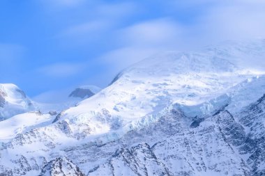 Parlak güneş ışığı, Mont Blanc 'ın karmaşık buzul oluşumlarını ve karla kaplı yamaçlarını vurguluyor. Berrak, sakin bir alp manzarası için canlı mavi gökyüzüne karşı..