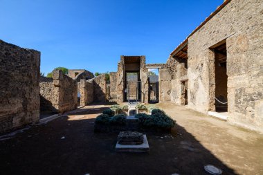 Pompeii, İtalya 'daki Venüs Evi' nde antik taş duvarları ve küçük manikürlü bahçesi olan açık hava avlusu. Parlak güneş ışığı, canlı mavi gökyüzünün altında desenli mason ve geometrik ekimi vurgular..