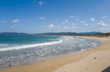 Kumlu sahil kıvrımları Kumihamacho 'daki Shotenkyo Sahili' nde hafif turkuaz dalgalarla karşılaşıyor. Uzak yeşil tepeler ve küçük bulutlarla kaplı parlak bir gökyüzü..