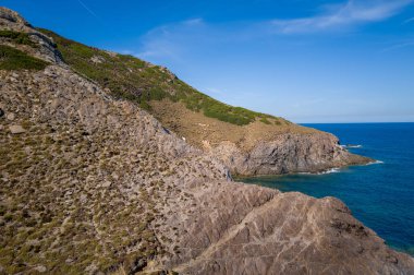Engebeli, kayalık uçurumların engebeli manzarası ve seyrek bitki örtüsü Arjantin yakınlarındaki derin mavi Akdeniz 'le buluşuyor. Güneş ışığı, açık bir gökyüzünün altında dokulu taş yüzeyleri ve dramatik kıyı şeridini vurgular..