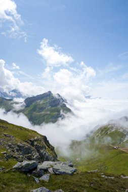 Pürüzlü kayalar ve çimenli yamaçlar Beaufortain 'deki dramatik bir alp vadisine göz yumar. Alçak bulutlar canlı mavi bir gökyüzünün altında yeşil tepelerin etrafında döner..