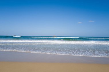 Kristal berrak sörf Kumihamacho 'daki Shotenkyo Sahili' nde parlak mavi gökyüzünün altında yavaşça süzülür. Açık deniz manzarası sakin ve ufukta uzak adacıklar var..