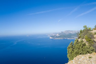 Canlı mavi Akdeniz, Cassis yakınlarındaki Calanques 'teki dramatik kireçtaşı kayalıklarının ve yemyeşil çimlerin altına uzanır. Açık gökyüzü ve parlak gün ışığı huzurlu ve geniş bir atmosfer yaratır..