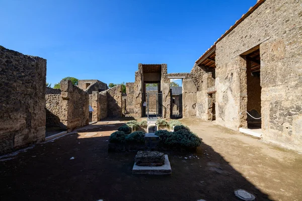 Pompeii, İtalya 'daki Venüs Evi' nde antik taş duvarları ve küçük manikürlü bahçesi olan açık hava avlusu. Parlak güneş ışığı, canlı mavi gökyüzünün altında desenli mason ve geometrik ekimi vurgular..