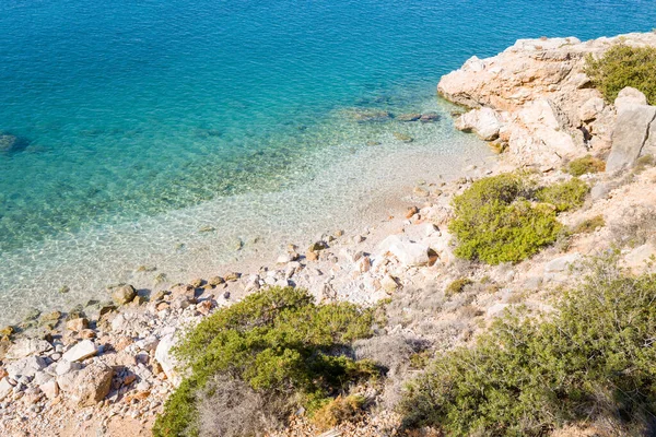 Kristal berraklığında turkuaz su, engebeli kayalık bir kıyı şeridine, seyrek yeşil çalılıklara ve güneş ışığında yanan taşlara çarpıyor. Parlak, davetkar sahne, Akdeniz 'in doğal dokularını ve canlı renklerini vurguluyor..