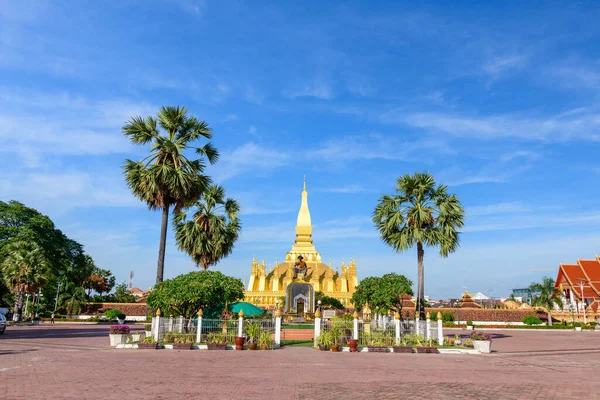 Luang 'ın, yüksek palmiye ağaçları ve açık mavi bir gökyüzü altında manikürlü bahçelerle çerçevelenmiş manzaralı bir meydanın ortasında duran ikonik altın bir stupa. Bu canlı sahne Laoss 'un çarpıcı mimarisini ve kültürel önemini vurguluyor.