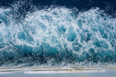 Akdeniz 'deki bir teknenin arkasında dönen turkuaz deniz köpüğünün yukarıdan görünüşü. Dinamik su dokuları ve canlı mavi renkler enerjik bir deniz soyutu oluşturur.