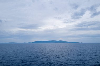 Sardunya kıyı şeridinin geniş bir görüntüsü sakin mavi su ve dramatik bulutlu gökyüzü sakin, dengesiz bir atmosfer yaratıyor..