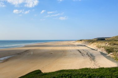 Plage de la Vieille eglise 'de geniş bir altın kum tabakası yumuşak dalgalar ve alçak çimenli kumullarla karşılaşıyor. Açık arazi, az miktarda bulutun mavi gökyüzüne dağılıp, huzurlu ve ferah bir atmosfer oluşturduğu yumuşak gün ışığıyla yıkanır..