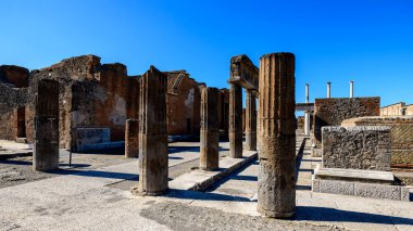 Pompeii, İtalya 'nın eski idari bölgesinde antik taş sütunlar ve tuğla duvarlar bulunuyor. Parlak güneş ışığı, parlak mavi gökyüzünün altında dokulu duvarcılık ve geometrik şekilleri aydınlatan keskin gölgeler bırakır..