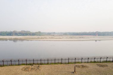 Yamuna Nehri 'nin durgun suları kumlu kıyıları ve Hindistan' ın Agra kentindeki uzak bir ağaç sınırını geçer. Puslu gökyüzü ve yumuşak sabah ışığı huzurlu ve huzurlu bir manzara yaratır..