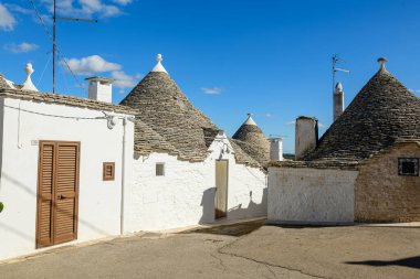 Alberobello, Apulia, İtalya 'da konik taştan çatıları olan bir grup bembeyaz trullo evi. Güneşli duvarcılık ve mavi gökyüzü benzersiz Akdeniz mimari tarzını ve desenli kireçtaşı yapısını ön plana çıkarıyor.