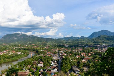 Luang Prabang şehrinin geniş panoraması yemyeşil tepeler ve kuzey Laos 'taki tropikal bitki örtüsü arasında yer almaktadır. Nam Khan nehri, parlak mavi bir gökyüzünün altında, etrafa dağılmış bulutlar eşliğinde, canlı bir Güneydoğu Asya manzarası yaratarak çevreyi sarıyor..