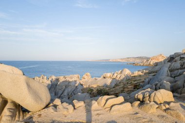 Yumuşak akşam güneşi, Capo Testa, Sardinya 'daki engebeli Akdeniz kıyıları boyunca uzanan pürüzsüz granit kayaları, engin mavi deniz ve berrak gökyüzü altındaki uzak uçurumlarla vurgular..