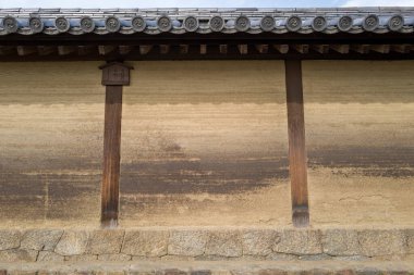 Horyuji, Nara 'da eski bir toprak duvarın yakın çekimi, katmanlı kil dokular, ahşap kirişler ve yumuşak gün ışığında geleneksel kiremitli çatı ayrıntıları içerir..