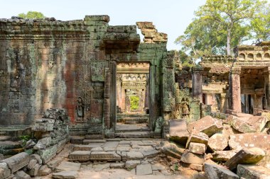 Antik taş geçitler ve Kamboçya Angkor bölgesindeki Preah Khan tapınağının yıpranmış kapıları yumuşak gün ışığıyla aydınlatılır. Sahnede yosunlu duvarcılık, karmaşık oymalar ve tropikal ağaçların arka planına kurulmuş harabeler yer alıyor..