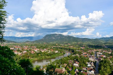 Panoramik manzara Luang Prabang şehrinin yemyeşil tepelerin arasına kurulduğunu ve Nam Khan nehrinin kuzey Laos 'ta dalgalandığını gösteriyor. Dramatik bulutlar ve canlı bitki örtüsü Güneydoğu Asya 'da canlı bir atmosfer yaratıyor.