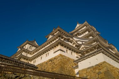 Ilık güneş ışığı, Himeji Kalesi 'nin katmanlı beyaz duvarlarını ve karmaşık kiremitli çatılarını vurguluyor..
