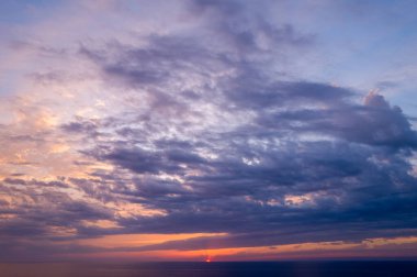 Güneş sakin Akdeniz 'in altına batarken mor ve şeftali rengi tonlarında geniş desenli bulutlar atmosferik bir alacakaranlık manzarası yaratıyor..