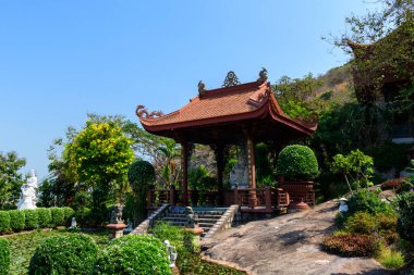 Karmaşık oymalarla süslü ahşap pavyon manikürlü çalılar, yemyeşil yeşillikler ve açık mavi gökyüzünün altında su zambaklarıyla dolu bir gölet ile çevrili bir taş platformun üzerinde duruyor. Barışçıl ortam heykel ve canlı heykellerle güçlendirilir.