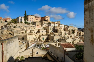 Kümelenmiş taş evler ve katmanlı çatılar Matera, İtalya 'da göz alıcı bir tepe manzarası oluşturuyor. Parlak güneş ışığı altında ve dağınık mavi bulutlu canlı bir gökyüzü..