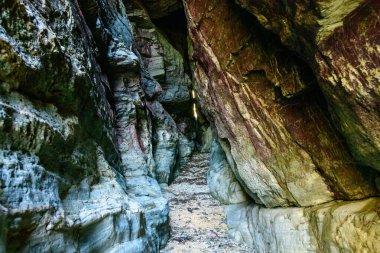 Cap de Carteret 'in engebeli taş duvarları arasında, dramatik dokular ve dağınık gün ışığında çok renkli kaya katmanlarının yer aldığı sıkı bir doğal koridor. Sahne bir gizem ve jeolojik tarih hissi veriyor..