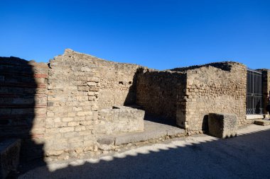 Antik taş ve tuğla duvarlar İtalya 'nın Pompeii kentindeki arkeolojik bölgede yıpranmış bir köşe oluşturuyor. Kıtır güneş ışığı geometrik gölgeleri canlı mavi bir gökyüzünün altında dokulu duvarlara yayar..