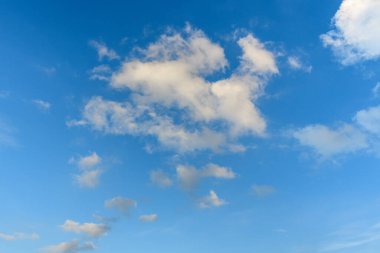 Dağılmış beyaz bulutlar açık mavi bir gökyüzünde sürükleniyor, ışık ve havadar bir atmosfer yaratıyor. Sahne, arka plan veya sakin kavramlar için ideal yumuşak bulut şekilleri ve açık alan içeriyor..