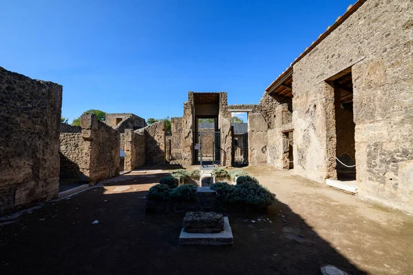 Antik taş duvarlar ve merkez bahçe yatağı Pompeii, İtalya 'daki Venüs Evi' nin açık avlusunu tanımlar. Kıtır sabah ışığı, yıpranmış duvarcılık ve kumlu zemin boyunca parlak mavi gökyüzünün altında keskin gölgeler bırakıyor..