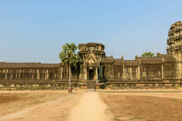 Angkor Vat, Kamboçya 'daki antik kumtaşı giriş köşkünün geniş görüşü bulutsuz mavi gökyüzüne karşı kurulmuştur. Tarihi Khmer yapısı, görkemli ve tropikal atmosferi vurgulayarak palmiye ağaçları ve kuru otlar tarafından çerçevelenmiştir..