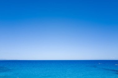 Minimalist deniz manzarası, canlı mavi gökyüzü ile Sardunya 'nın Baunei kenti yakınlarındaki Akdeniz' in sakin turkuaz sularıyla buluşuyor. Ufuk kıtır kıtır ve manzara dinginlik ve açıklık yayıyor..