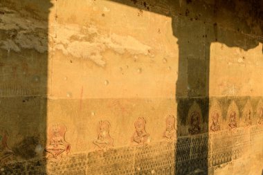 Ilık güneş ışığı, Angkor Vat 'taki yıpranmış kumtaşı bir duvarın üzerinde kalın geometrik gölgeler bırakır ve bir dizi karmaşık apsara oymalarını ortaya çıkarır. Dokulu yüzey ve ritmik ışık bu ikonik Kamboçya tapınağının tarihi Khmer sanatını çağrıştırıyor..