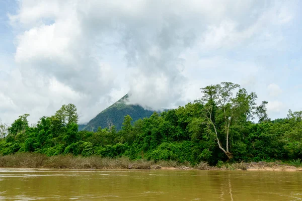 Yoğun bulutlar kuzey Laos 'taki Nam Ou Nehri' nin yukarısındaki ormanlı bir dağın zirvesinde toplanıyor. Yoğun yeşil ağaçlar ve vahşi bitki örtüsü nehir kıyısında parlak bir gökyüzünün altında canlı bir doğal manzara yaratıyor..