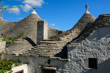 Geleneksel konik kireçtaşı kireç taşı kiremitleri ve beyaz bacalı trullo çatıları Alberobello, Apulia, İtalya 'da canlı mavi bir gökyüzünün altında duruyor. Dokulu yüzeyler ve geometrik formlar benzersiz Akdeniz mimari mirasını vurguluyor.