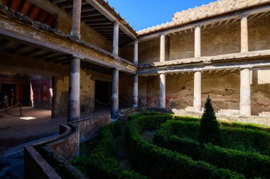 İtalya, Pompeii 'deki Aşıklar Evi' nin iç avlusunu manikürlü bir çit ve merkezi bir çalı doldurur. Antik taş sütunlar, yıpranmış duvarlar ve solmuş freskler berrak mavi gökyüzünün altında sakin bir Roma ayarı yaratır..