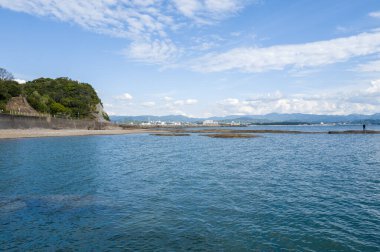 Temiz mavi su, Japonya 'nın Tanabe kenti yakınlarında dağınık bulutlarla dolu bir gökyüzünün altında yeşil uçurumlar ve uzak şehir manzaralı engebeli bir kıyı şeridiyle kesişiyor. Huzurlu deniz manzarası ufuktaki dağlar tarafından çerçevelenir..