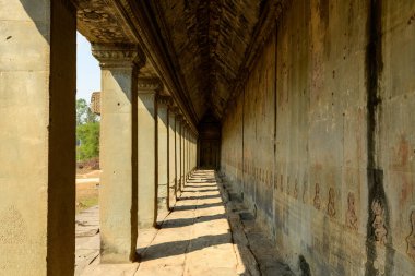 Angkor Vat 'taki uzun kumtaşı galerisi gün ortası güneş ışığıyla aydınlatılarak zemin ve duvar boyunca karmaşık levrek kabartmalarıyla süslenmiş ritmik gölgeler oluşturdu. Antik Khmer mimarisi ve dokulu yüzeyler tarih ve geometrik hissi uyandırıyor.