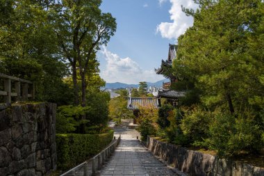 Kyoto 'daki Chion-in tapınağının çatısına uzanan yemyeşil yemyeşil merdivenlerle çevrili güneşli taş basamaklar, mavi gökyüzü altında uzak dağlar ve dağınık bulutlar..