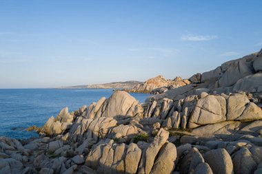 Sardunya 'nın Capo Testa kentindeki sakin mavi suların üzerinde, berrak bir gökyüzünün altında sıcak güneş ışığıyla yıkanan pürüzsüz granit kayalar..