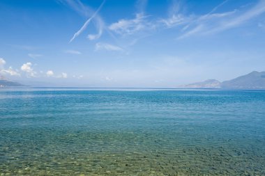 Sakin, şeffaf su ön planda bir çakıl taşını gözler önüne seriyor. Argolide, Peloponnese 'deki Psifta plajında geniş bir turkuaz denizi ve açık mavi gökyüzünün altındaki uzak dağlara açılıyor..