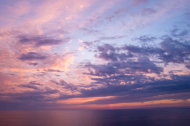 Pembe, lavanta ve mavi tonlarda narin bulutlar, gün batımında, huzurlu Akdeniz sularının üzerinde gökyüzünde süzülüyor. Yumuşak ışık ve yumuşak renk eğimleri sakin, atmosferik bir deniz manzarası yaratır..
